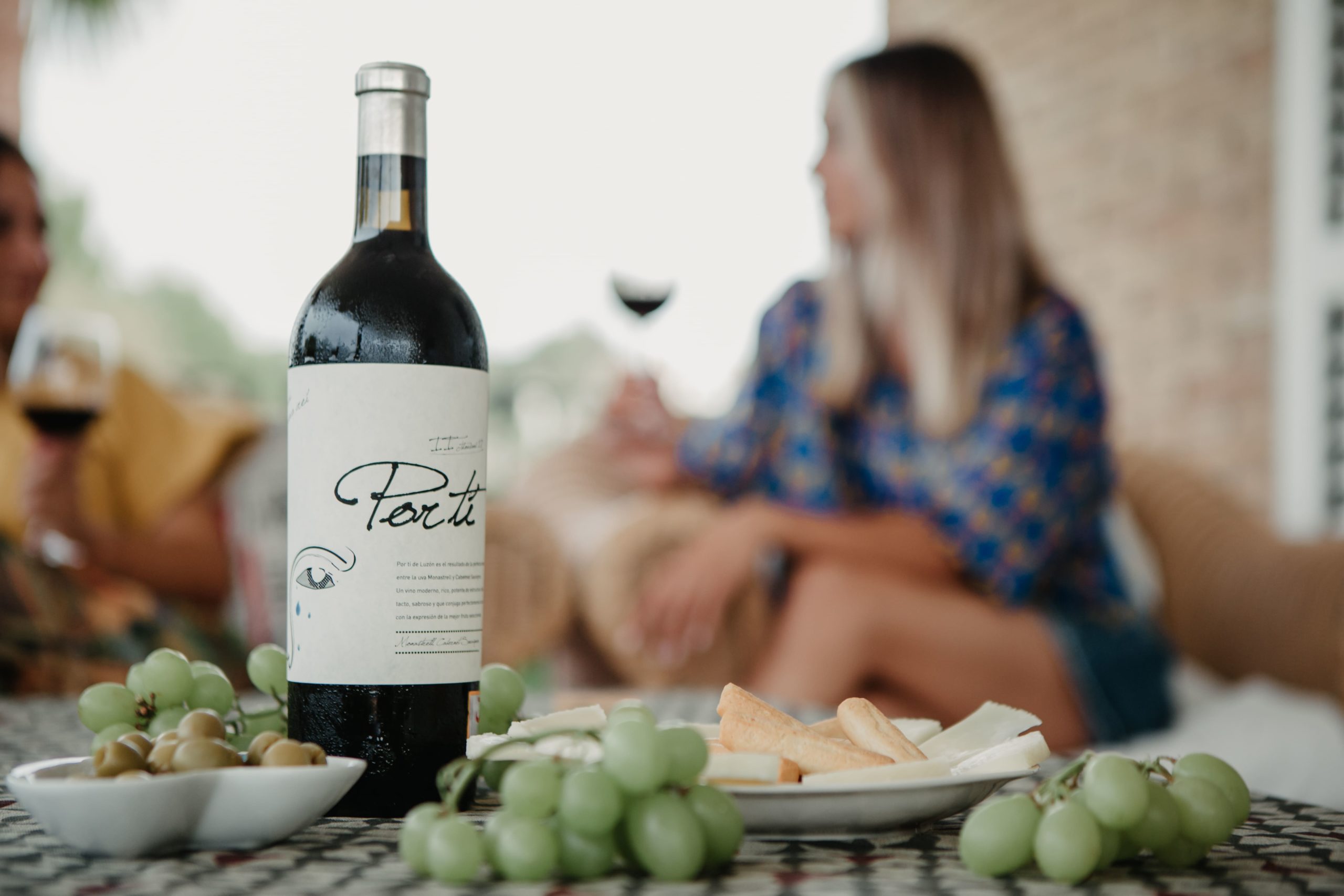 A bottle of Por Tí from Bodegas Luzón with out-of-focus women behind it